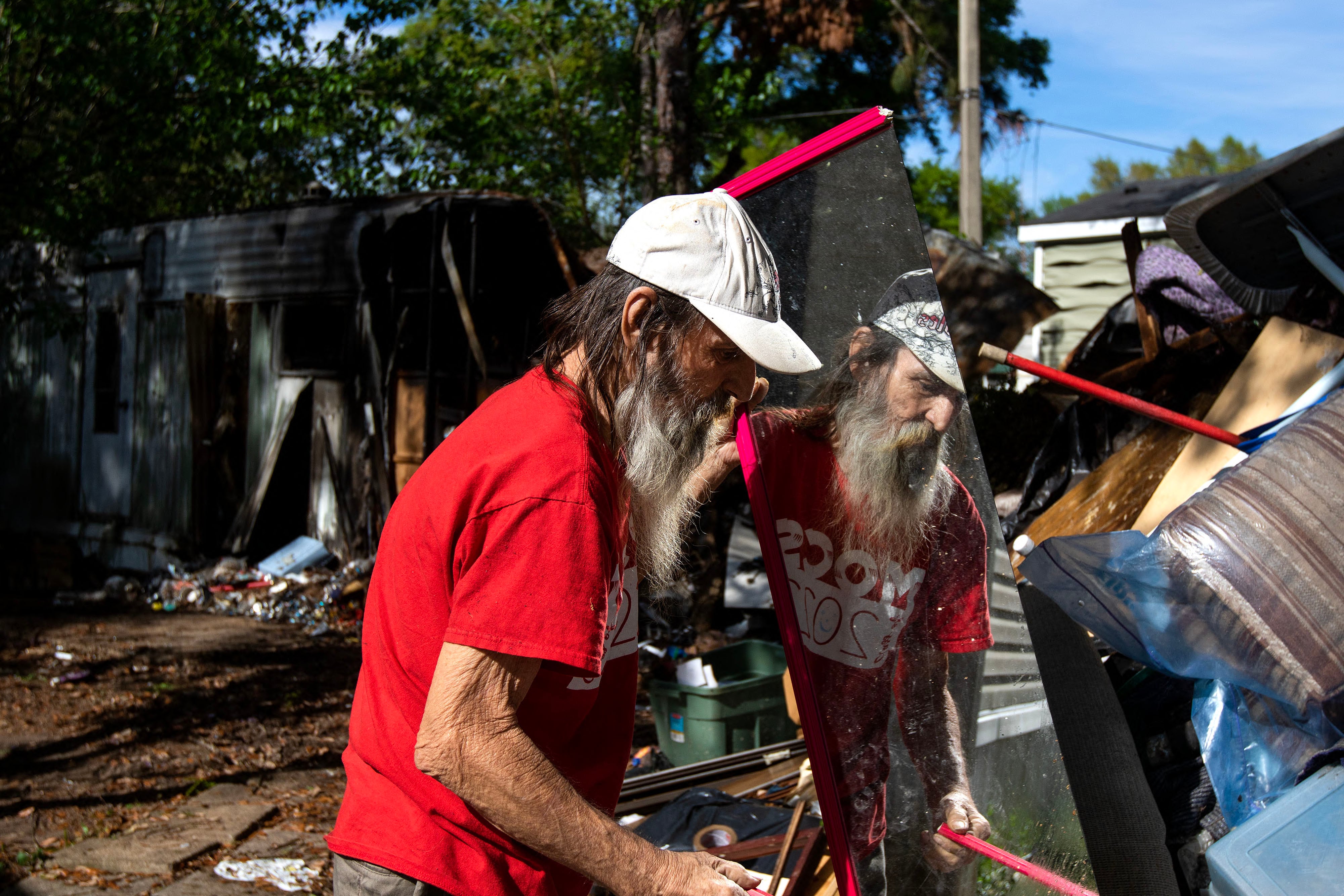 Paul Patchin pulls a mirror out of the wreckage of his burned mobile home at Lake Bradford...